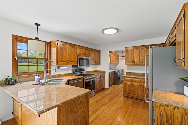 N39W32890 High Hill Ct, Nashotah, WI 53058 - kitchen featuring appliances with stainless steel finishes, washer and clothes dryer, a sink, a peninsula, and light wood-style flooring