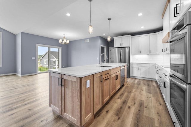 1407 Ridgetrail Dr, Cross Plains, WI 53528 - kitchen featuring a center island with sink, appliances with stainless steel finishes, a chandelier, light wood-style flooring, and decorative backsplash