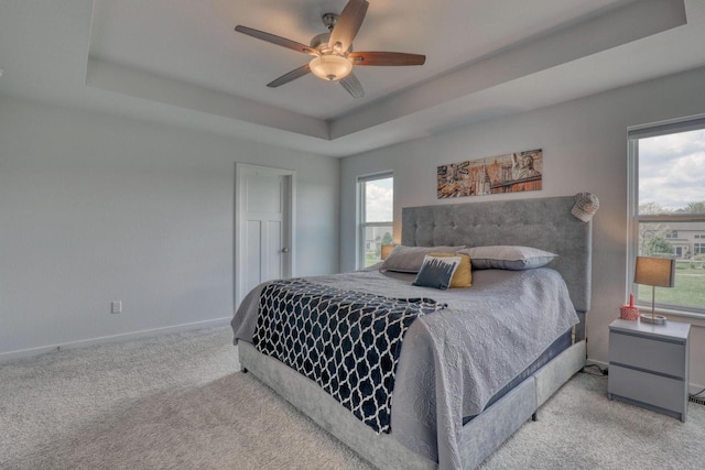 carpeted bedroom featuring a tray ceiling, baseboards, and ceiling fan