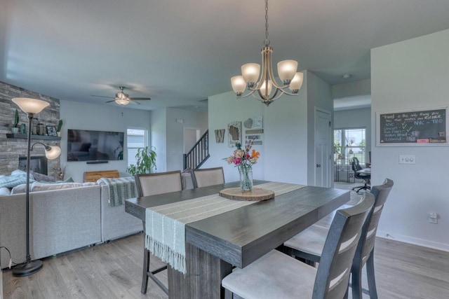 dining space featuring ceiling fan, light wood-style floors, stairs, a chandelier, and baseboards