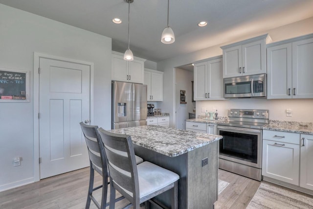 kitchen with appliances with stainless steel finishes, a kitchen island, light wood-style flooring, light stone countertops, and recessed lighting