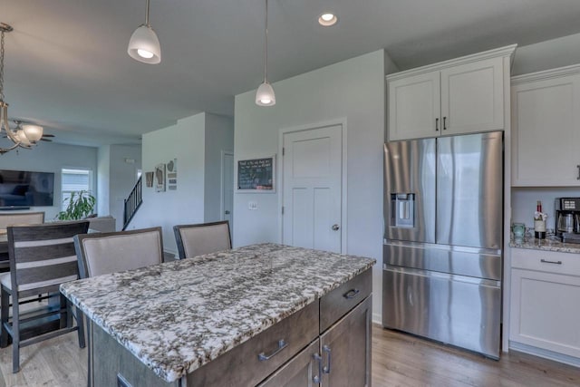 kitchen featuring stainless steel fridge, light stone countertops, light wood finished floors, and a center island