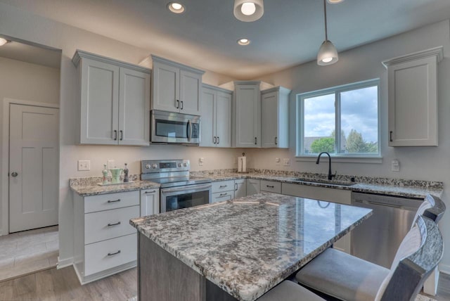 kitchen with appliances with stainless steel finishes, a sink, light stone counters, a kitchen breakfast bar, and recessed lighting