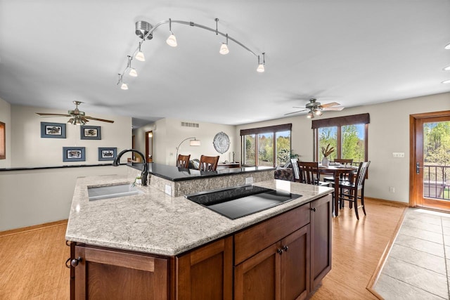 169003 Shorewood Dr, Rosholt, WI 54473 - kitchen with black electric cooktop, a ceiling fan, a sink, light wood-style floors, and an island with sink