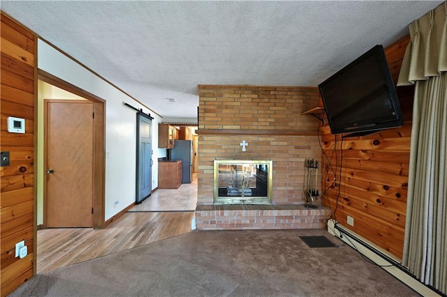 811 Russell St, Grantsburg, WI 54840 - unfurnished living room with a baseboard heating unit, a brick fireplace, a textured ceiling, a barn door, and light wood finished floors