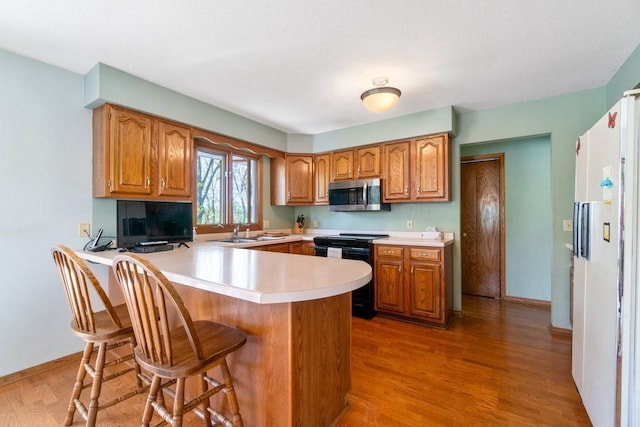 kitchen featuring electric range, stainless steel microwave, a peninsula, freestanding refrigerator, and light countertops