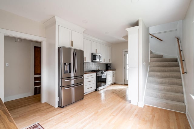 kitchen with stainless steel appliances, backsplash, white cabinets, and light wood-style floors