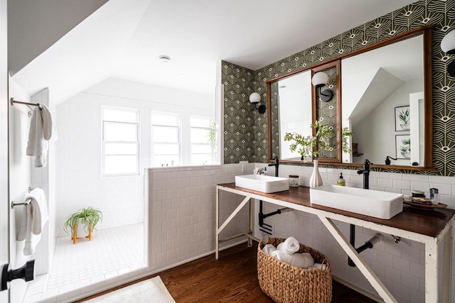 full bathroom with wood finished floors, a walk in shower, lofted ceiling, tile walls, and double vanity