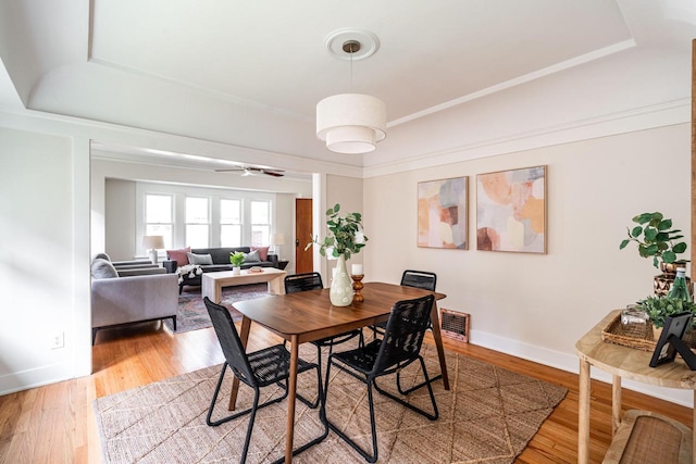 dining area with a raised ceiling, a ceiling fan, light wood finished floors, and baseboards