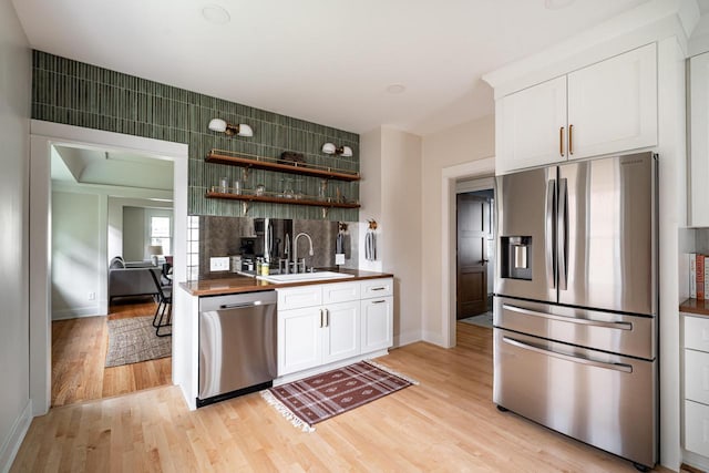 kitchen featuring appliances with stainless steel finishes, a sink, light wood finished floors, white cabinetry, and baseboards