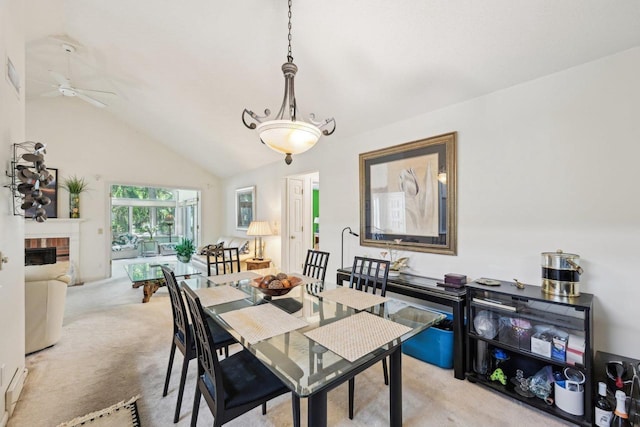 dining room with ceiling fan, light colored carpet, a fireplace, and vaulted ceiling