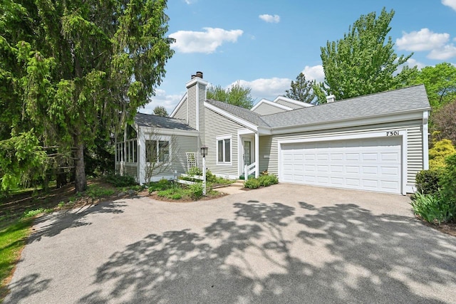 view of front of house with driveway, a chimney, an attached garage, and roof with shingles