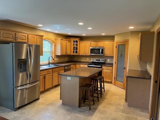 1030 Woodland Ct, Plover, WI 54467 - kitchen with appliances with stainless steel finishes, a sink, dark countertops, a kitchen bar, and a kitchen island