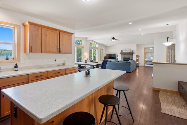 12450 Nixon Rd, Minocqua, WI 54548 - kitchen featuring ceiling fan, a fireplace, dark wood-style floors, a kitchen breakfast bar, and a center island