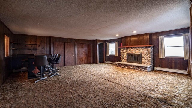 N2145 Lind Center Rd, Waupaca, WI 54981 - unfurnished living room with wooden walls, a baseboard heating unit, carpet flooring, a stone fireplace, and a textured ceiling