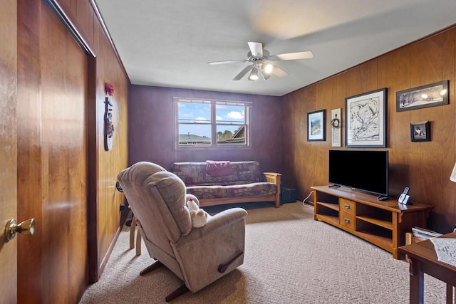carpeted living area with ceiling fan and wood walls