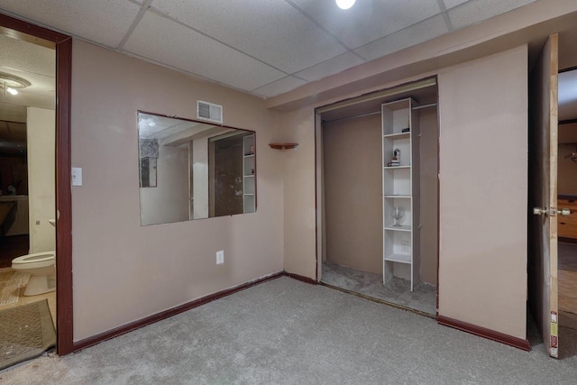 unfurnished bedroom featuring a closet, carpet, a paneled ceiling, and baseboards