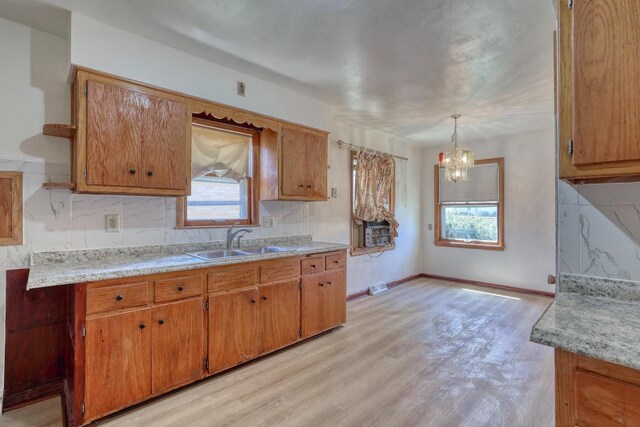 kitchen with a sink, light wood-type flooring, a chandelier, light countertops, and decorative backsplash