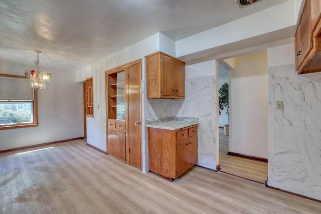 kitchen with light wood-type flooring, a chandelier, light countertops, brown cabinetry, and baseboards