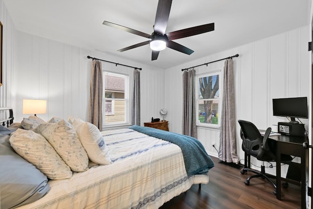 bedroom with a decorative wall, multiple windows, dark wood-type flooring, and ceiling fan