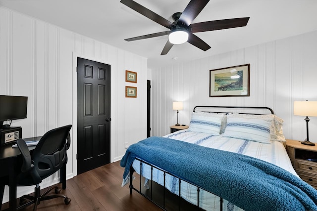 bedroom featuring dark wood-style flooring, an office area, a decorative wall, and ceiling fan