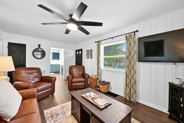 living area featuring ceiling fan, wood finished floors, and a decorative wall