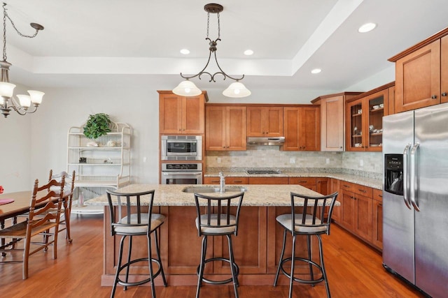 2140 Prairie View Pt, Lake Geneva, WI 53147 - kitchen with stainless steel appliances, a sink, brown cabinets, under cabinet range hood, and a tray ceiling