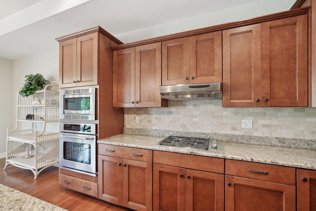 2140 Prairie View Pt, Lake Geneva, WI 53147 - kitchen with stainless steel appliances, brown cabinetry, under cabinet range hood, light wood finished floors, and backsplash