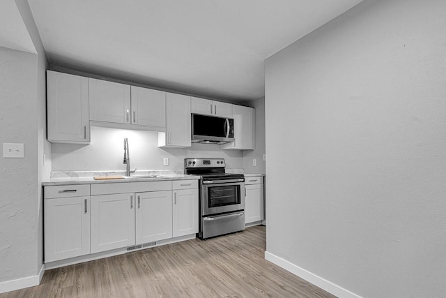 1629 Kentucky Ave, Sheboygan, WI 53081 - kitchen with appliances with stainless steel finishes, a sink, baseboards, light wood finished floors, and a textured wall