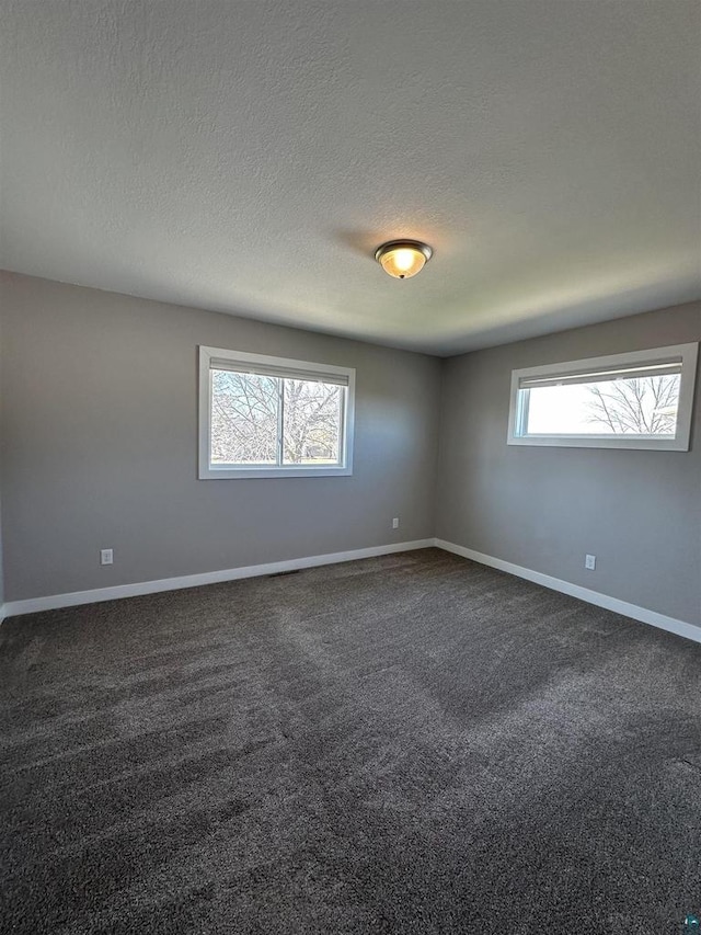 spare room with dark carpet, baseboards, and a textured ceiling