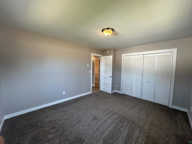 unfurnished bedroom featuring baseboards, dark colored carpet, and a closet