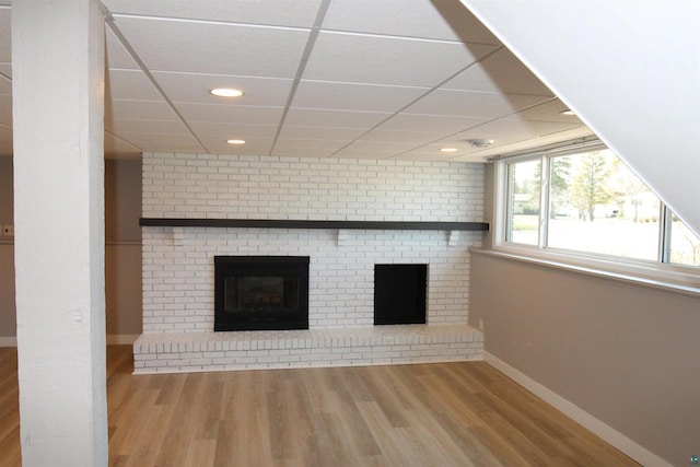 unfurnished living room featuring a brick fireplace, baseboards, wood finished floors, recessed lighting, and a drop ceiling