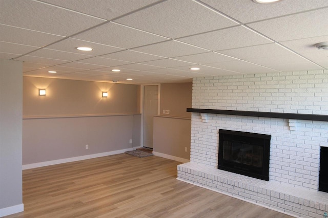 unfurnished living room with baseboards, wood finished floors, a brick fireplace, a drop ceiling, and recessed lighting