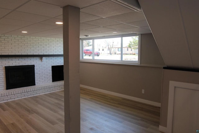 empty room featuring baseboards, wood finished floors, recessed lighting, a brick fireplace, and a paneled ceiling