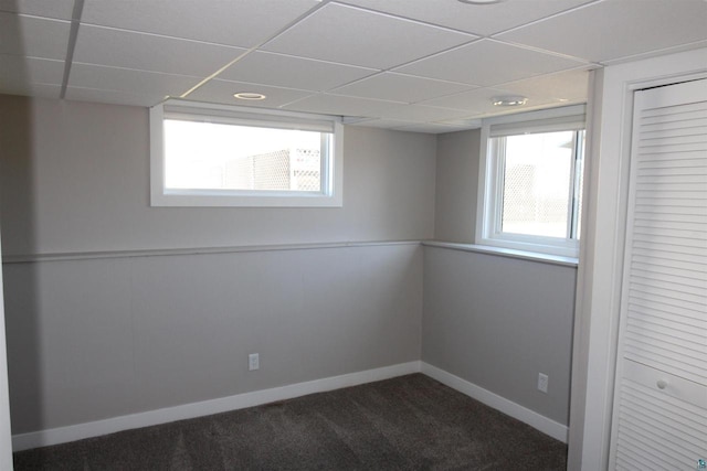 below grade area featuring dark colored carpet, a paneled ceiling, and baseboards