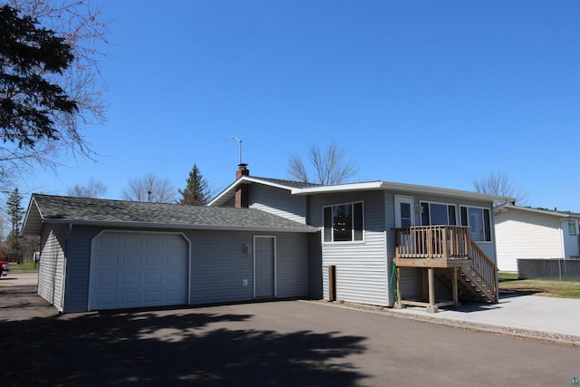 view of front of home with asphalt driveway, stairs, a shingled roof, a garage, and a chimney