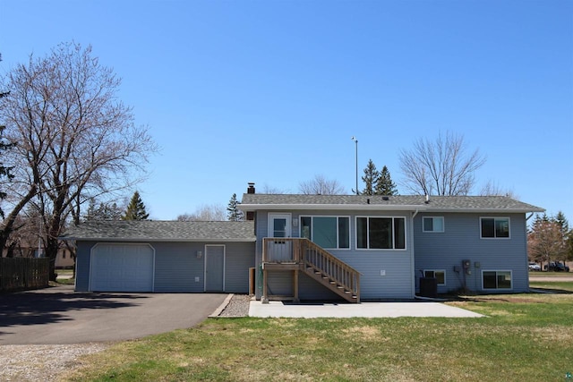 rear view of property with a chimney, a yard, driveway, central AC unit, and a garage