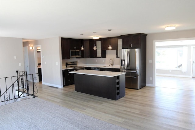 kitchen with stainless steel appliances, a sink, light countertops, light wood-type flooring, and a kitchen island