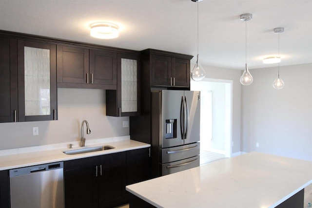 kitchen featuring appliances with stainless steel finishes, a sink, pendant lighting, dark brown cabinets, and glass insert cabinets