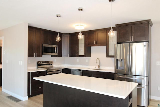 kitchen featuring appliances with stainless steel finishes, a sink, dark brown cabinets, light countertops, and baseboards