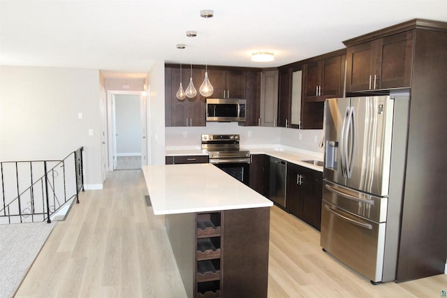 kitchen featuring appliances with stainless steel finishes, dark brown cabinetry, light wood-style floors, light countertops, and a kitchen island