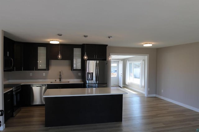 kitchen with appliances with stainless steel finishes, a sink, light countertops, wood finished floors, and a center island