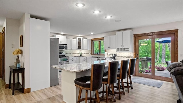 E3313 Jennifer Ln, Eau Claire, WI 54701 - kitchen with appliances with stainless steel finishes, a kitchen breakfast bar, decorative backsplash, light wood-style flooring, and white cabinetry
