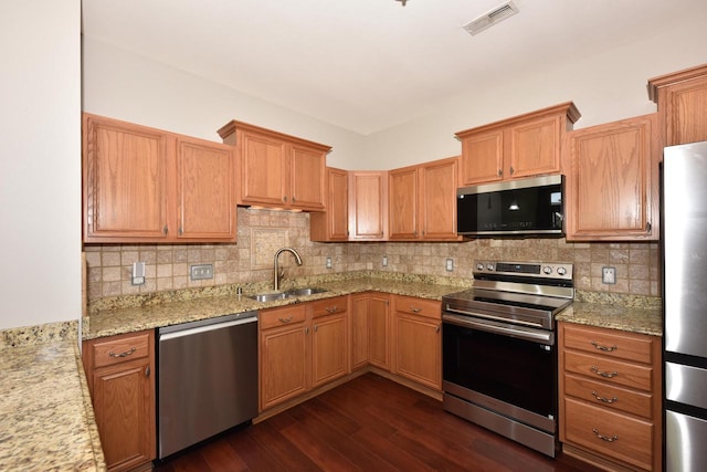 kitchen featuring appliances with stainless steel finishes, a sink, dark wood-type flooring, light stone countertops, and tasteful backsplash