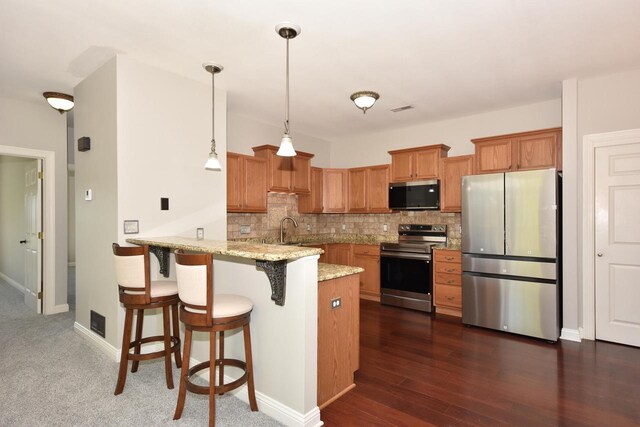 kitchen with stainless steel appliances, a peninsula, a sink, tasteful backsplash, and brown cabinetry