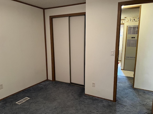 unfurnished bedroom featuring a heating unit, dark carpet, crown molding, a textured ceiling, and a closet