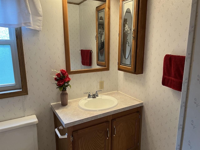 half bathroom with toilet, vanity, and wallpapered walls