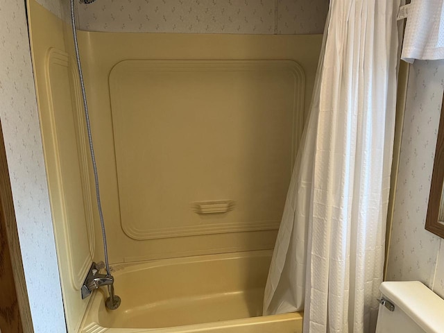 bathroom with wallpapered walls, toilet, and shower / bath combination with curtain