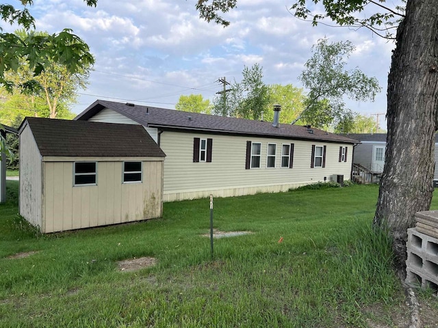 rear view of property with a shed, an outbuilding, a lawn, and central AC unit