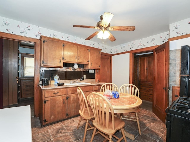 kitchen with black gas range, a ceiling fan, light countertops, brown cabinets, and wallpapered walls